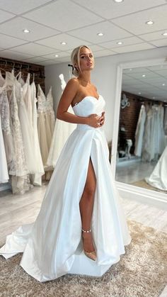 a woman standing in front of a mirror wearing a white dress with high slits