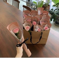 a hand holding a bouquet of roses on top of a wooden table next to a brown paper bag