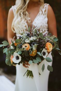 a woman holding a bouquet of flowers and greenery in her hands, wearing a white dress