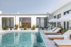 an outdoor swimming pool with chaise lounges and umbrellas next to the house