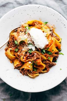 a white plate topped with pasta covered in sauce and sour cream next to a fork