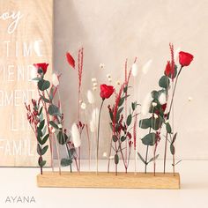 red and white flowers are arranged in a wooden vase on a table next to a sign