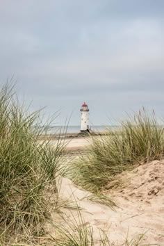 a light house sitting on top of a sandy beach next to tall grass and sea oats