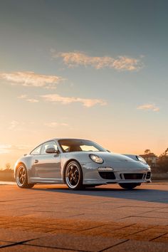 a white sports car parked on the side of a road in front of a sunset