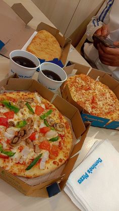 two pizzas sitting on top of a table next to coffee cups and napkins