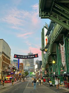 people are walking down the street in front of some shops and buildings at sunset or dawn