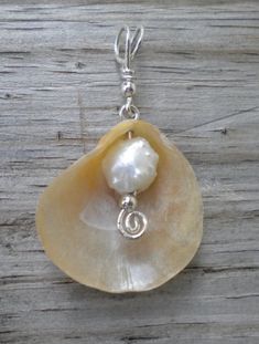 a large shell with a pearl in the center on a silver chain hanging from a wooden surface