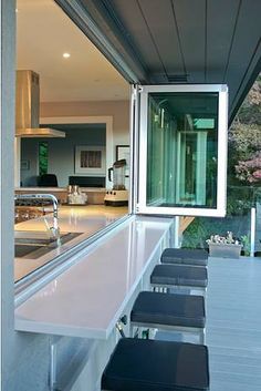 an outdoor kitchen with bar stools next to the counter top and windows on the outside wall