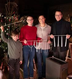 three people and a child holding up clothes pins in front of a christmas tree with presents on it