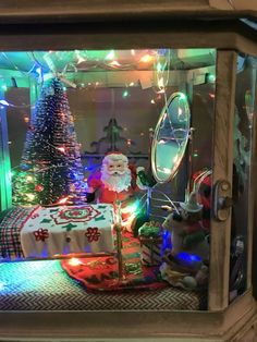 a christmas display in a glass case with lights and decorations on the table next to it