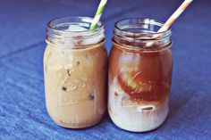 two mason jars filled with iced coffee on a blue tablecloth, one is empty and the other has straws in it