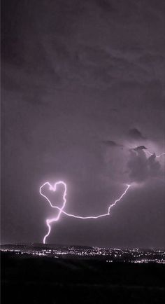 a lightning bolt is seen in the sky over a city at night with dark clouds