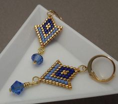 a white plate topped with two blue and gold beaded earrings on top of each other