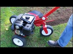 a man standing next to a red and black lawn mower on top of grass