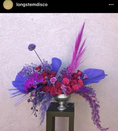 a vase filled with purple and red flowers sitting on top of a wooden table next to a wall