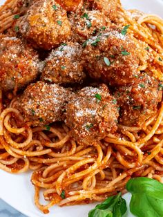 spaghetti with meatballs and parmesan cheese is on a white plate, garnished with fresh basil