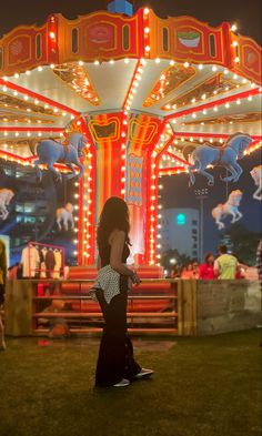 a woman standing in front of a merry go round ride at night with lights on