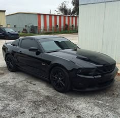 a black sports car parked in front of a storage building on the side of a road