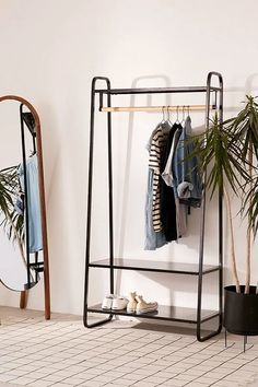 a rack with clothes hanging on it next to a mirror and potted palm tree