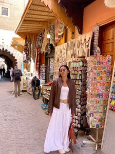 a woman standing in front of a store with lots of items on display behind her