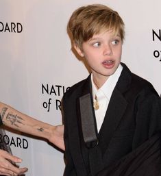 a young boy in a suit and tie standing next to an older woman with tattoos on her arm