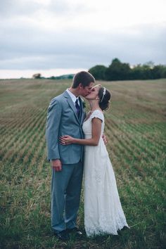 a bride and groom kissing in the middle of an open field with rows of crops behind them