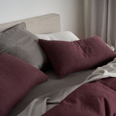 an unmade bed with red and grey pillows