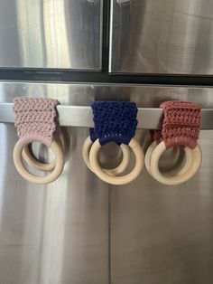 three crocheted wooden rings hang on a stainless steel refrigerator door handle with handles