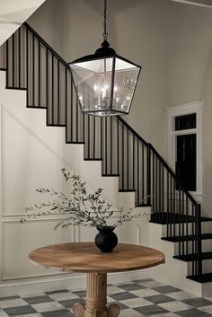 a table with a vase on it in front of a stair case and chandelier