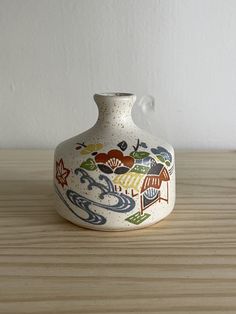 a white vase sitting on top of a wooden table next to a wall and floor