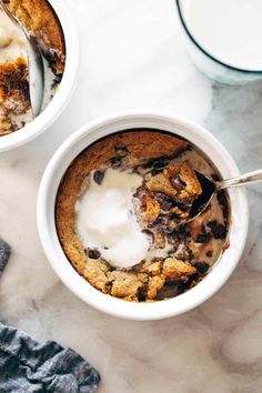 two white bowls filled with dessert on top of a marble counter next to a glass of milk