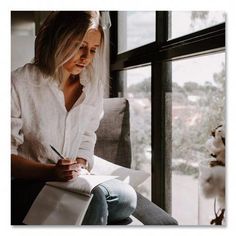 a woman sitting on a window sill writing