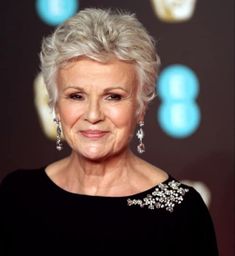 an older woman with grey hair smiling at the camera and wearing earrings on her head