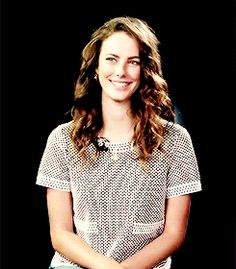 a woman standing in front of a black background with her arms crossed and looking at the camera