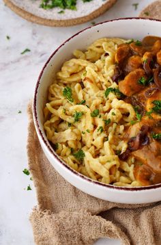 a white bowl filled with pasta and mushrooms on top of a table next to bread