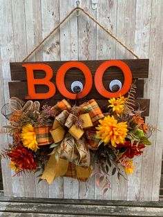 a door hanger decorated with fall flowers and an orange boo sign hanging on a wooden wall