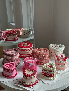 a table topped with lots of cakes covered in pink and red frosting on top of a white cake plate