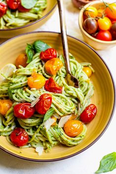 two bowls filled with pesto pasta and cherry tomatoes on top of a white table