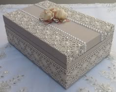 a decorative box is sitting on a table with white lace and flowers in it's center