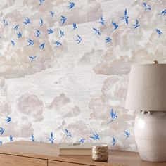 a white vase sitting on top of a wooden table next to a wallpaper covered in blue birds