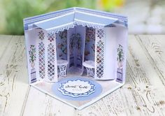 a paper doll house with furniture and flowers on the front, sitting on a wooden table