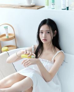 a young woman sitting on top of a white couch holding a yellow object in her hand