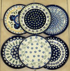 six plates with blue and white designs sitting on a tile floor in front of a tiled wall