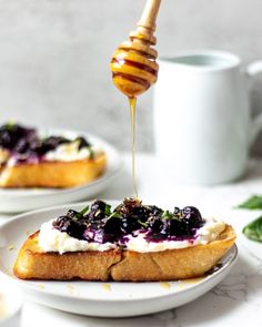 a piece of bread with blueberry sauce being drizzled over it on a white plate