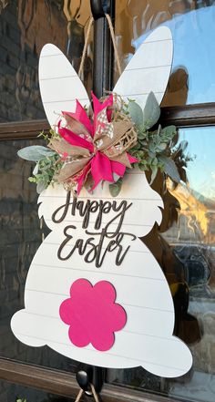 a sign that says happy easter hanging on a door with a bow and some flowers