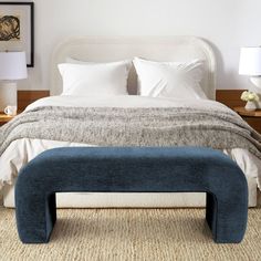 a bed with white linens and blue footstool in front of a night stand