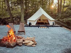 a tent set up in the middle of a forest with fire pit and chairs around it