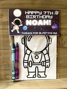 a birthday card with an astronaut and two crayons in front of it on a wooden surface