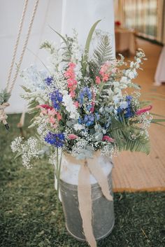 a vase filled with lots of flowers sitting on top of a grass covered field next to a rope