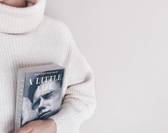 a person wearing a white sweater holding a book in their hands and looking at the camera